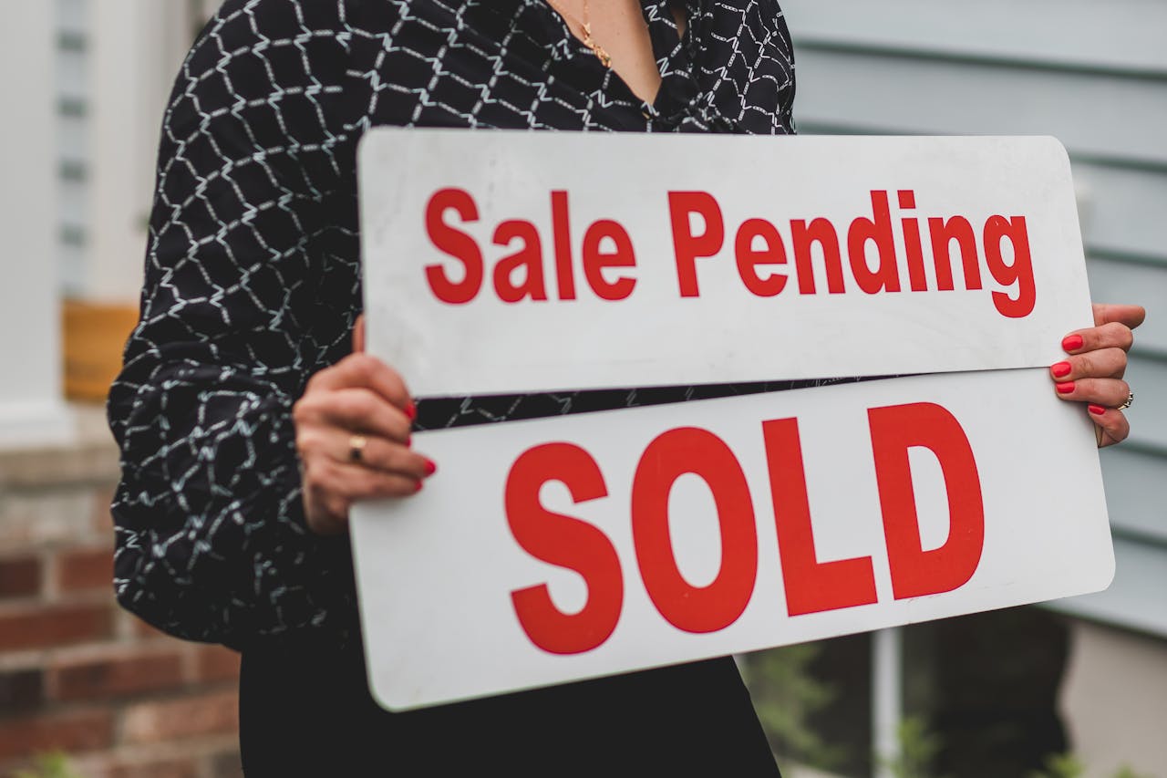 gallery-4 A businesswoman holding 'Sale Pending' and 'Sold' signs indicating a successful real estate transaction.