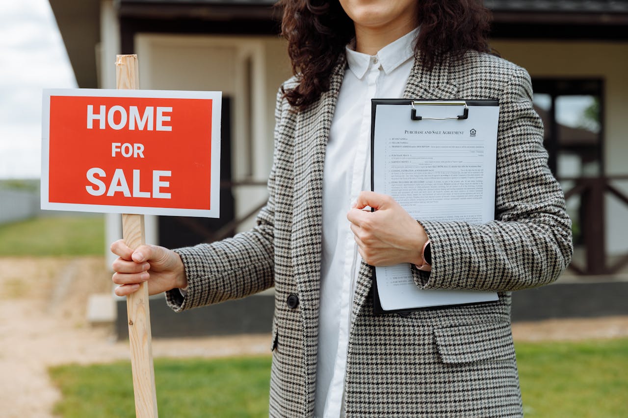 gallery-5 A real estate agent holding a home for sale sign and clipboard outside a property.